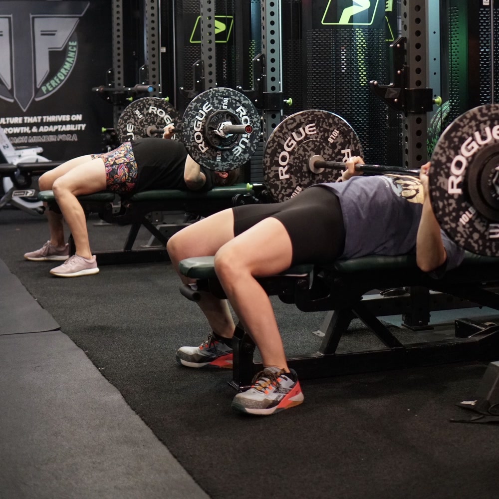 Two members bench pressing side by side in a small group class